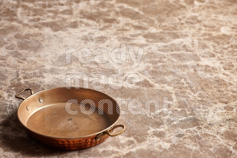A small copper pan on beige marble background