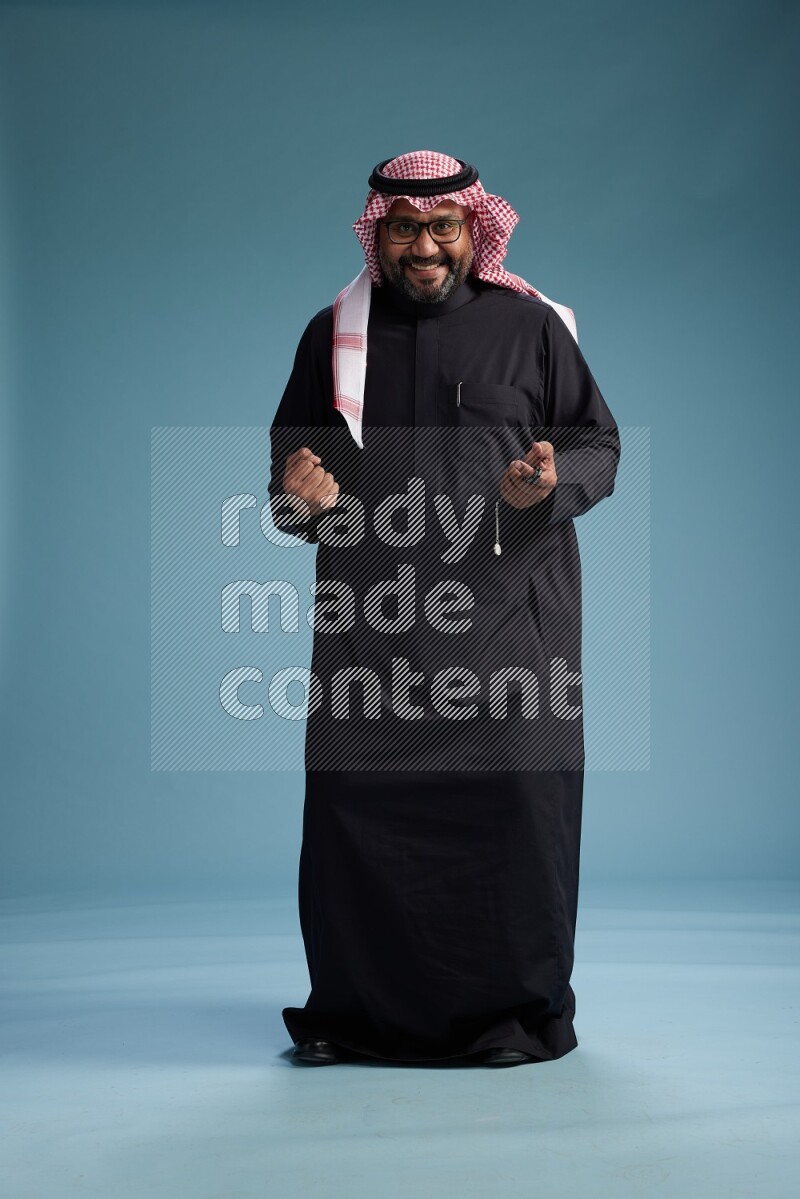 Saudi Man with shimag Standing Interacting with the camera on blue background