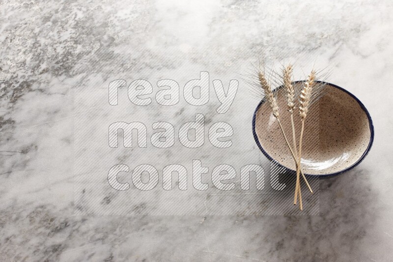 Wheat stalks on multicolored pottery bowl on grey marble background