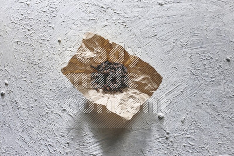 Cloves on crumpled piece of paper on a textured white flooring