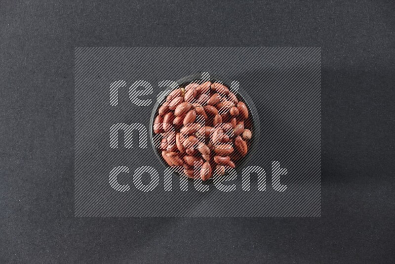 A black pottery bowl full of red skin peanuts on a black background in different angles