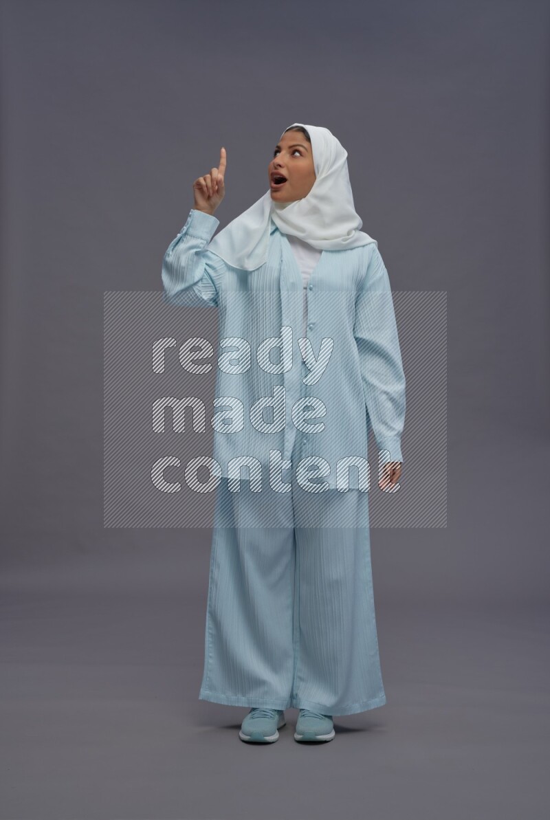 Saudi woman wearing hijab clothes standing interacting with the camera on gray background