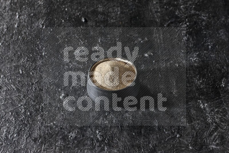 وعاء فخار أسود مملوء ببودرة الفلفل الأبيض على أرضية سوداء