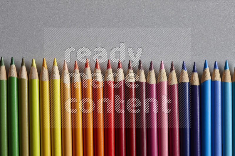 A collection of colored pencils arranged showcasing a gradient of different hues on grey background