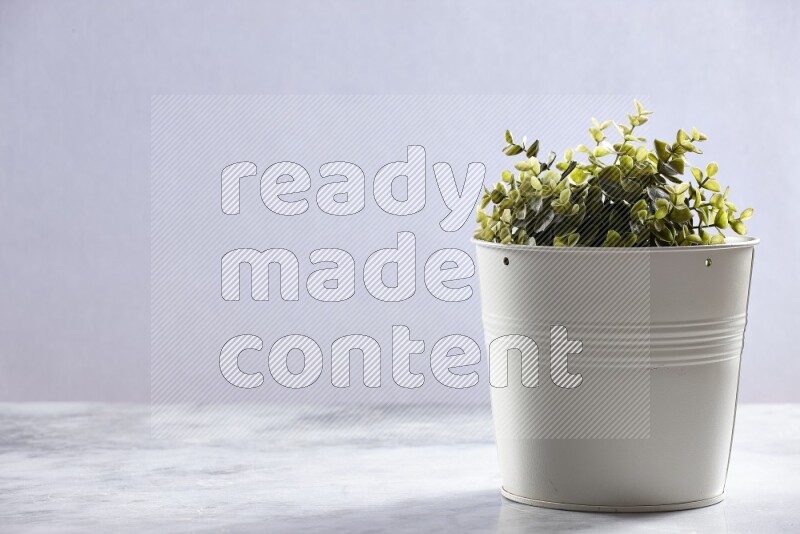 Green artificial plant in white pot on grey marble background