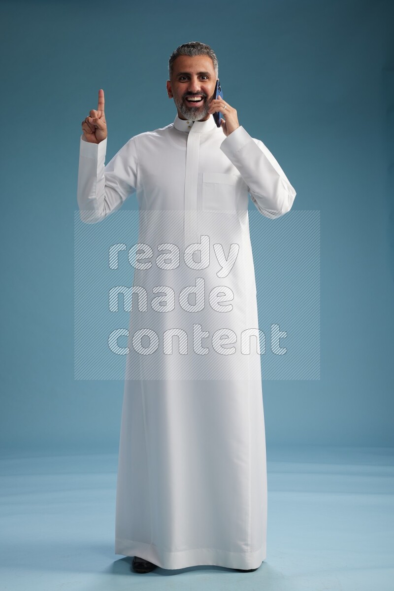 Saudi man wearing thob talking on the phone on blue background
