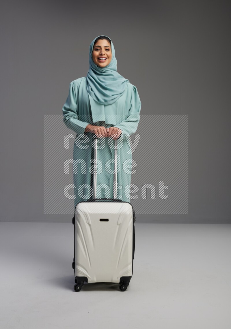 Saudi Woman wearing Abaya standing holding Travel bag on Gray background