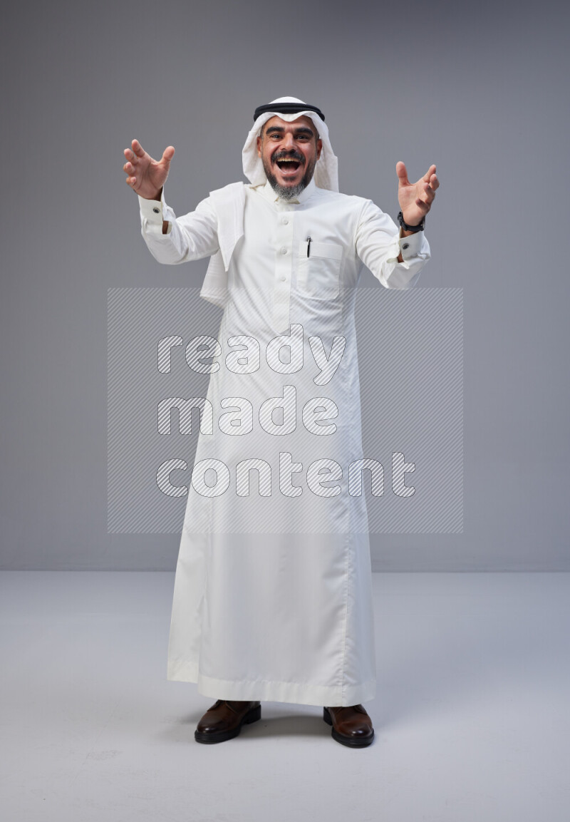 Saudi man Wearing Thob and white Shomag standing interacting with the camera on Gray background