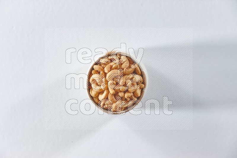 A beige ceramic bowl full of cashews on a white background in different angles