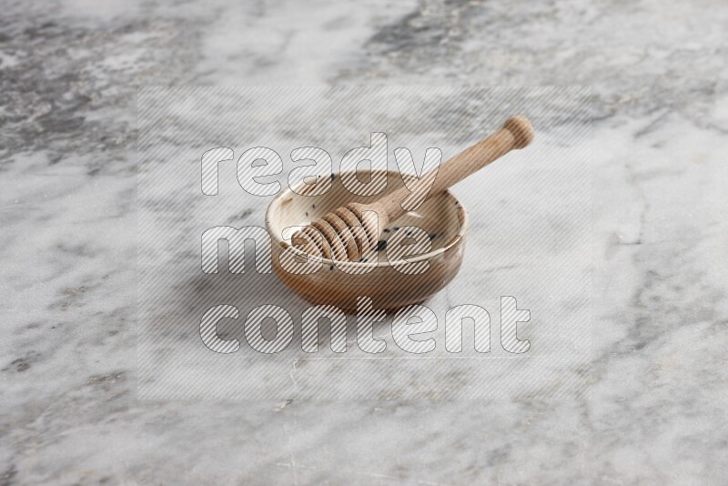 Multicolored pottery bowl with wooden honey dipper in it on grey marble background