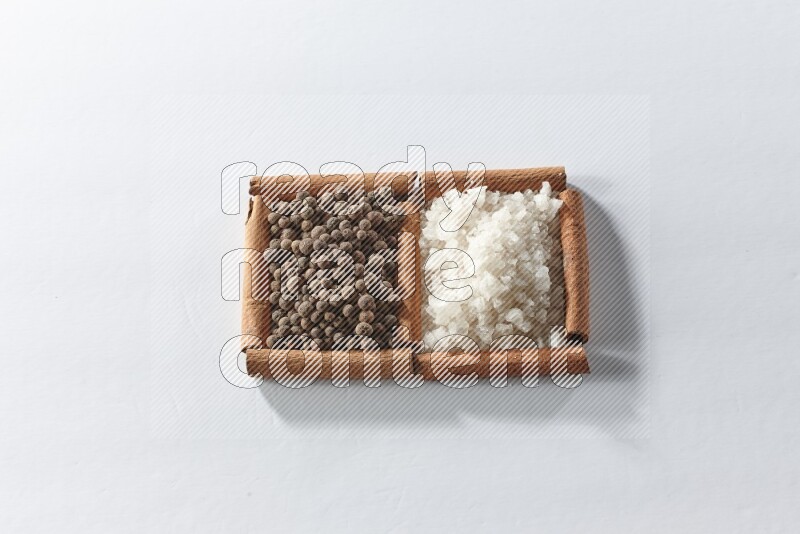 مربعان من أعواد القرفة ممتلئان بالملح الأبيض وحبوب الفلفل الحلو علي خلفية بيضاء