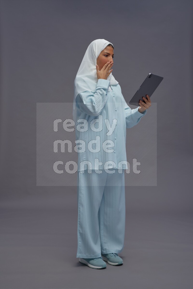 Saudi woman wearing hijab clothes standing working on tablet on gray background