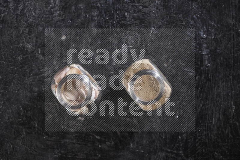 وعاءان زجاجيان احدهما ممتلئ ببودرة الثوم والأخر ممتلئ بفصوص الثوم علي خلفية سوداء