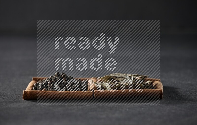 مربعان من أعواد القرفة ممتلئان بحبوب الفلفل الأسود وأوراق الغار علي خلفية سوداء