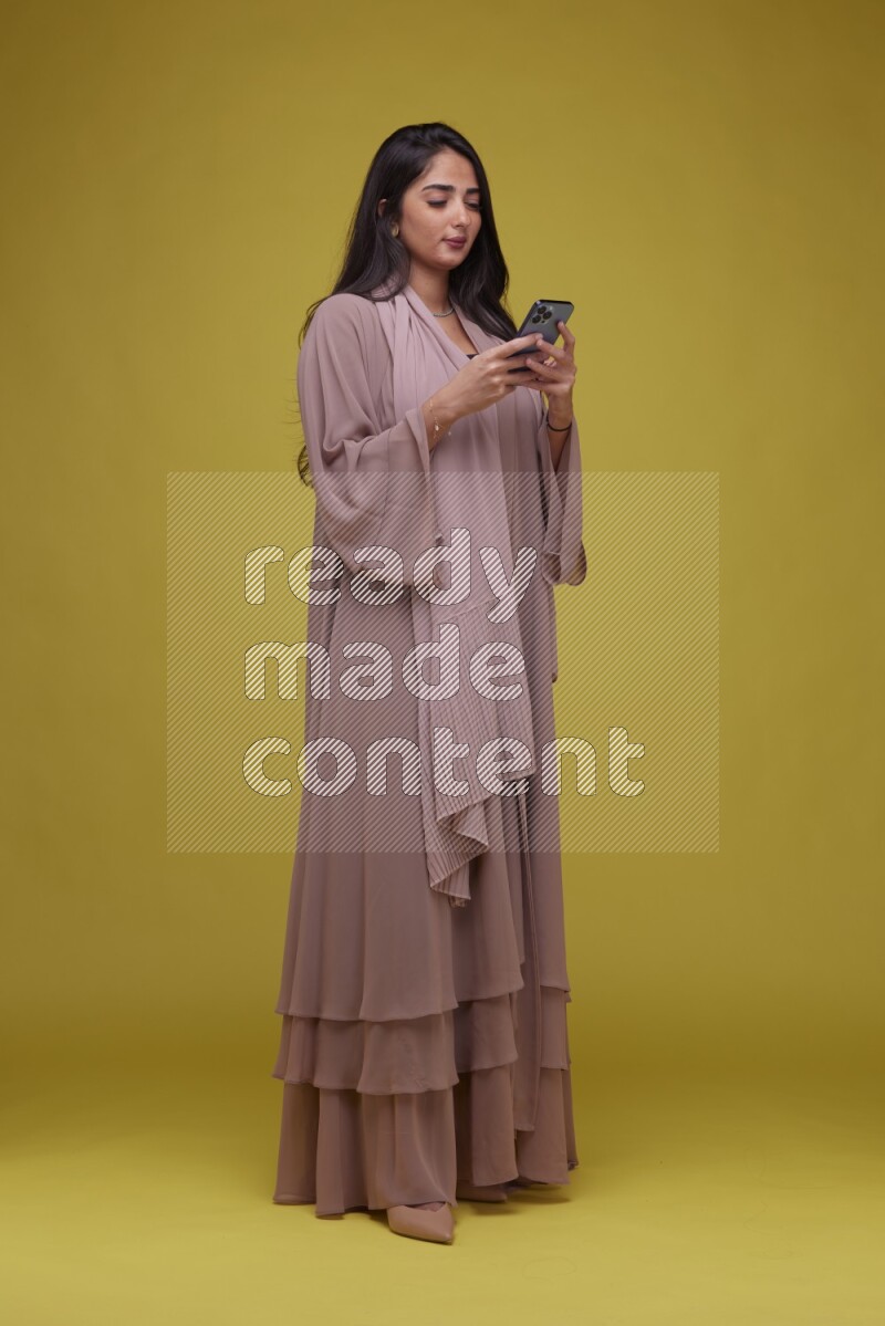 A woman Texting on a Yellow Background wearing Brown Abaya