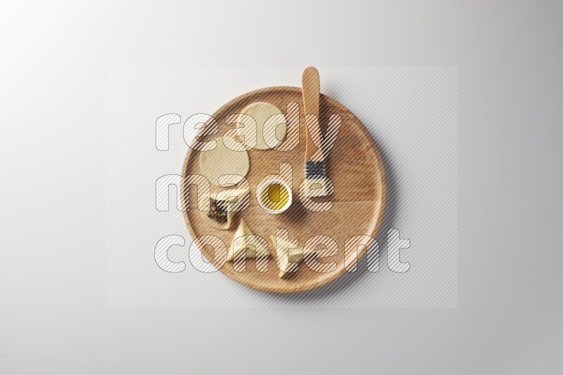 two closed sambosas and one open sambosa filled with meat while oil with oil brush aside in a wooden dish on a white background