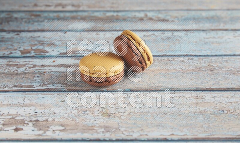 45º Shot of two Yellow and Brown Chai Latte macarons on light blue wooden background