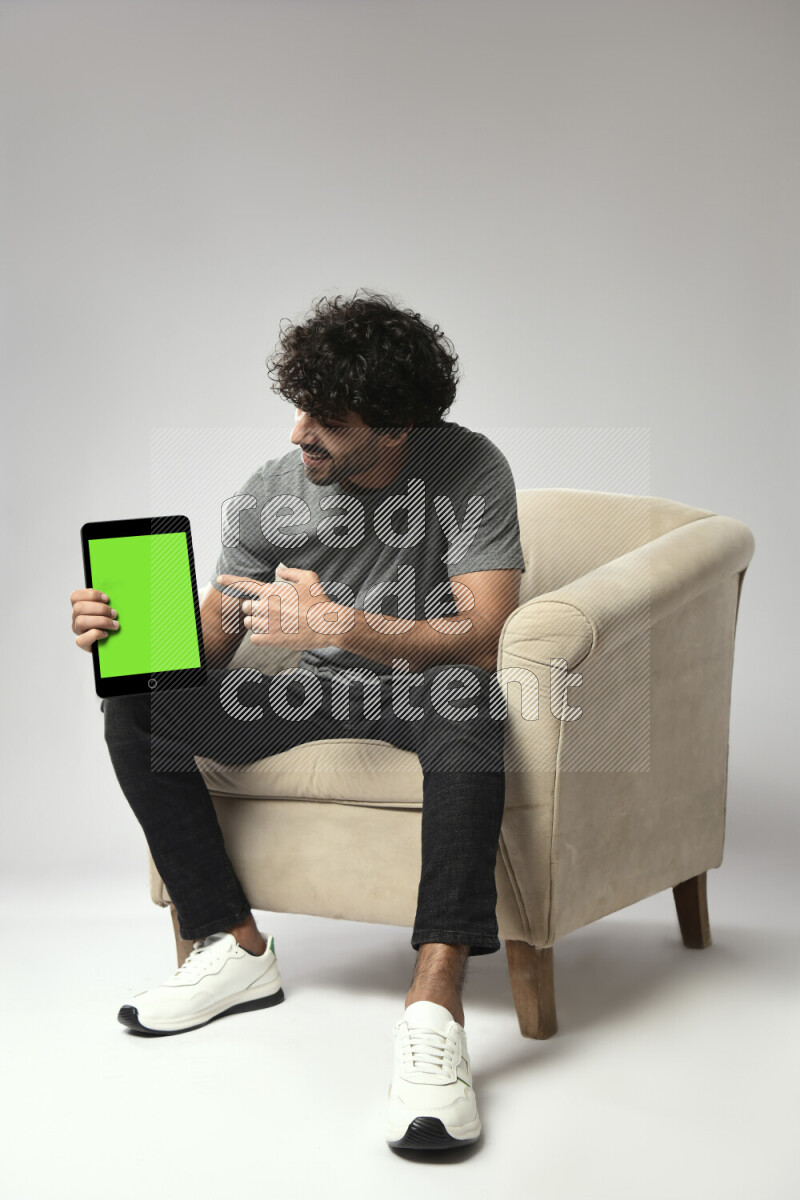 A man wearing casual sitting on a chair showing a tablet screen on white background