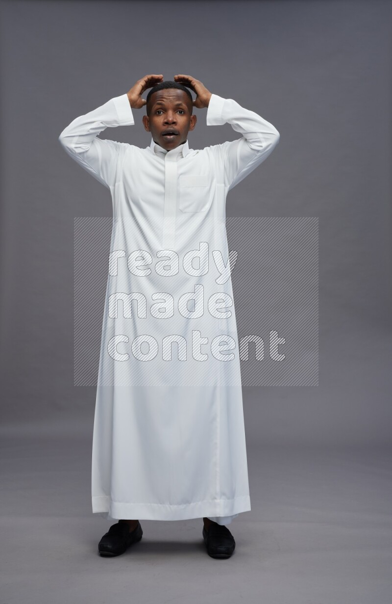 Saudi man wearing thob standing hands behind head on gray background