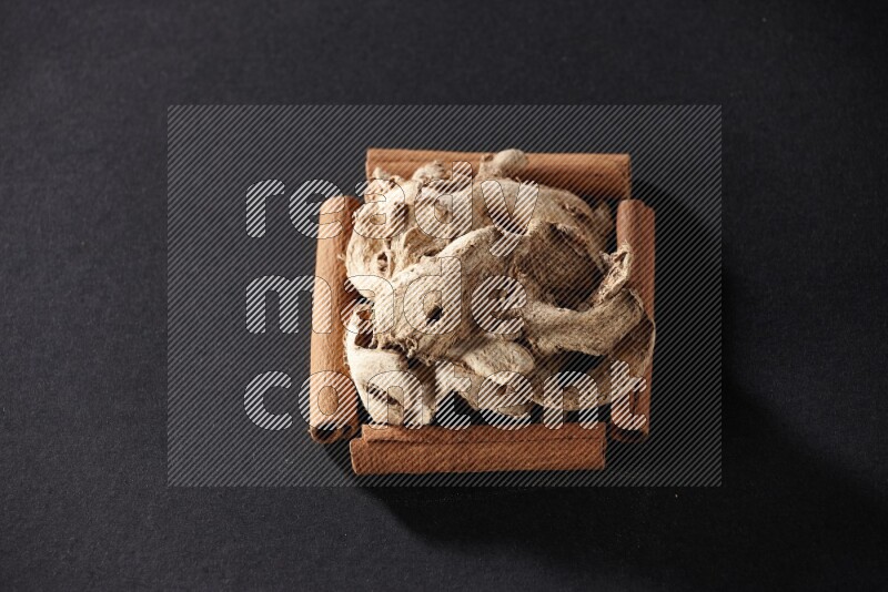 أربعة من أعواد القرفة مكونة شكل مربع بداخلها زنجبيل مجفف علي خلفية سوداء