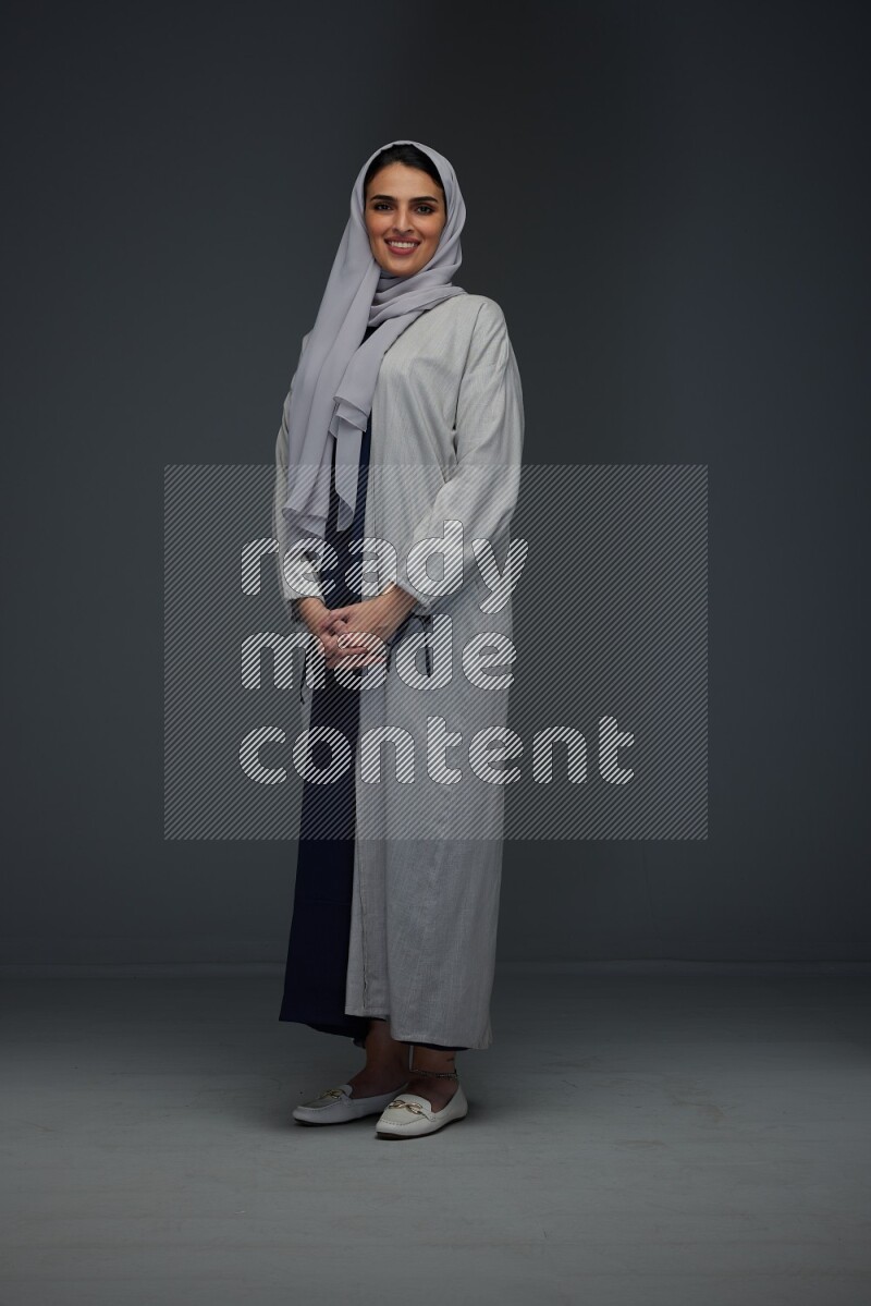 A Saudi woman wearing a light gray Abaya and head scarf standing and making multi poses eye level on a grey background