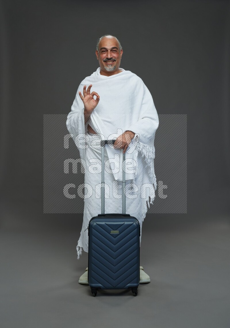 A man wearing Ehram Standing holding traveling bag on gray background