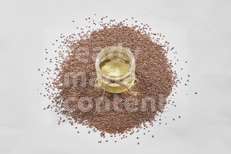 A glass jar full of flaxseeds oil surrounded by flax seeds on a white flooring