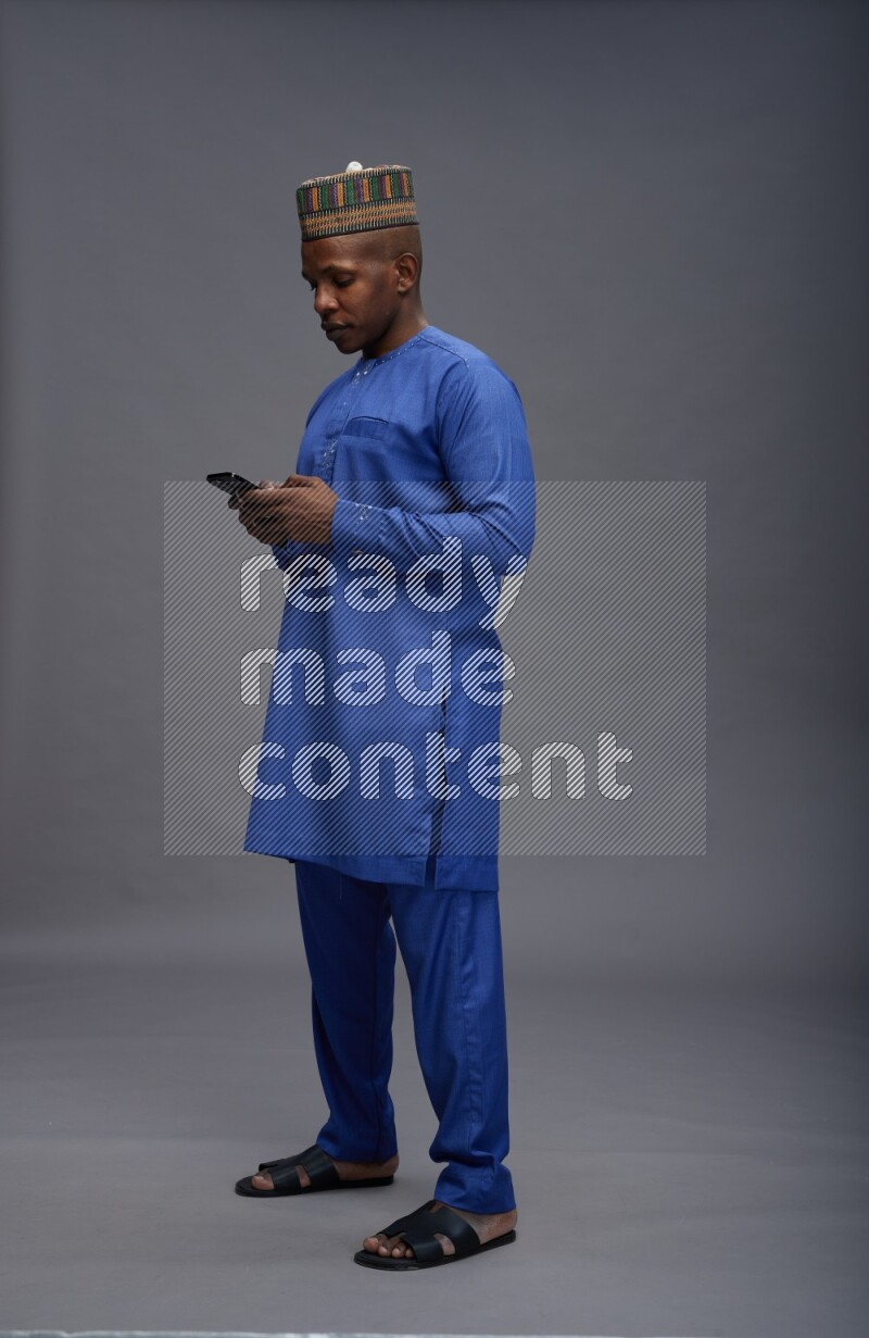 Man wearing Nigerian outfit standing texting on phone on gray background