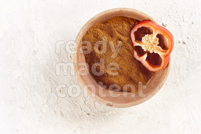 A wooden bowl full of ground paprika powder on white background