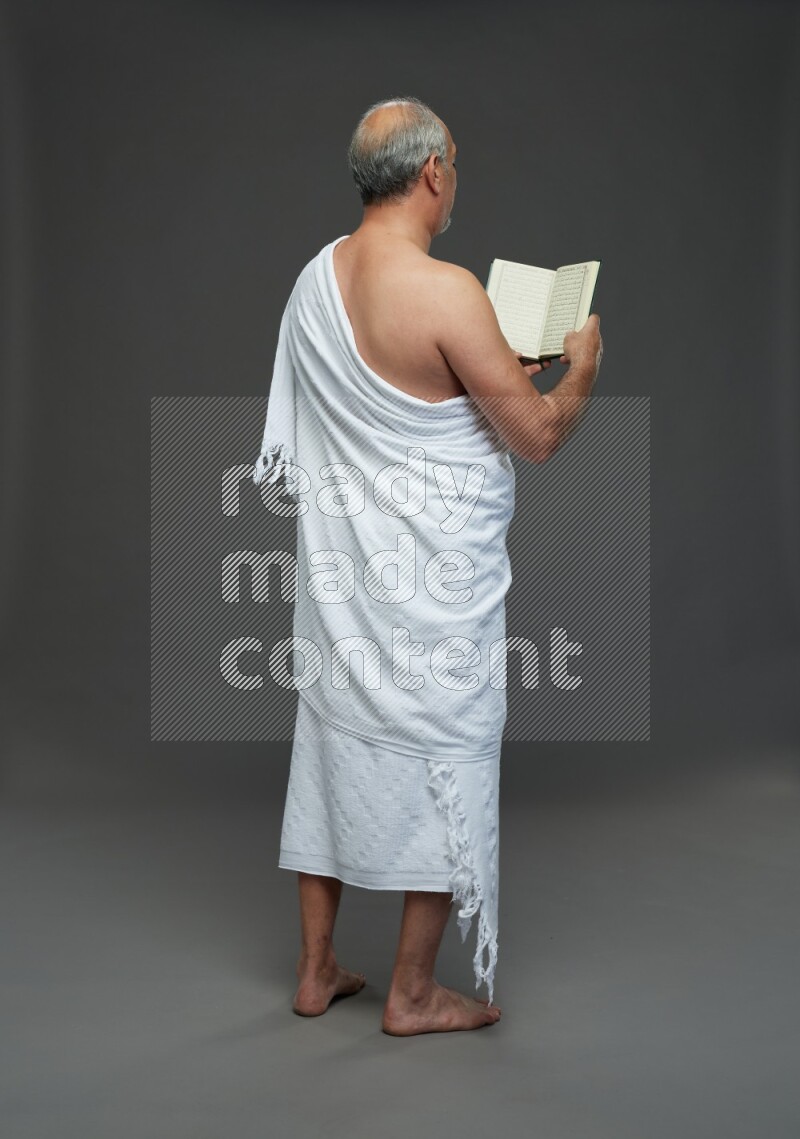 A man wearing Ehram Standing reading quran on gray background
