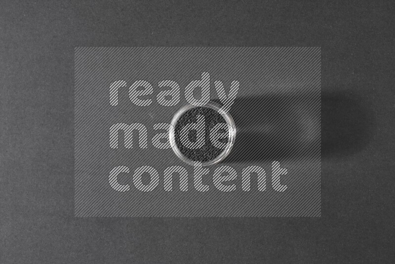 A glass jar full of black seeds on a black flooring