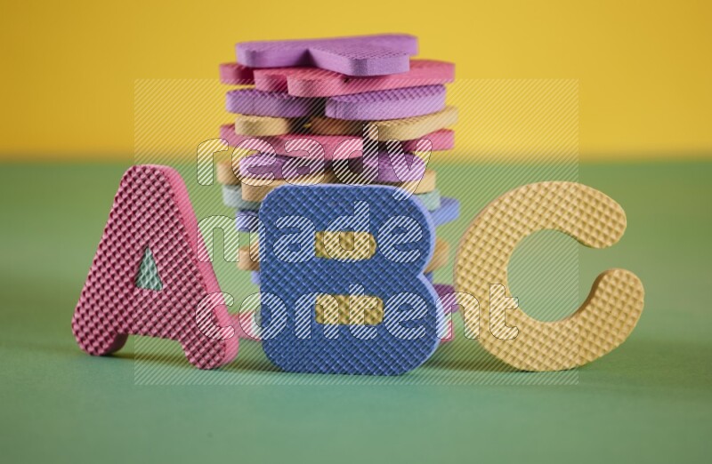 مجموعة من حروف الأبجدية الملونة المصنوعة من الفوم على خلفية صفراء وخضراء (ألعاب للأطفال)