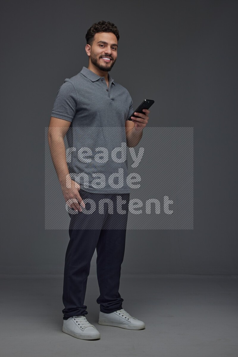 A man wearing casual standing and using his phone eye level on a gray background