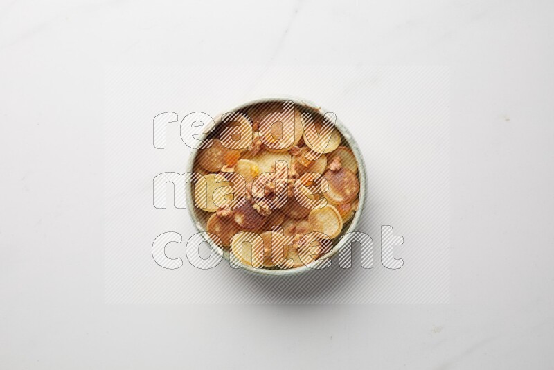 Top-view shot of walnut and apricot cereal pancakes in a round bowl on white background