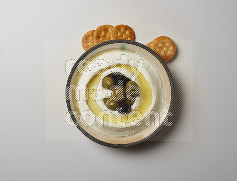 Lebnah garnished with whole black olives in a pottery plate on a white background