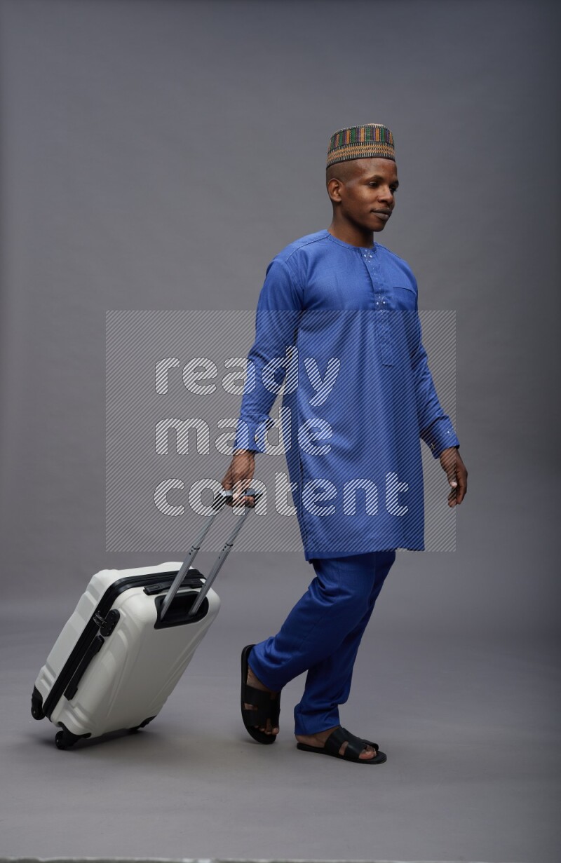 Man wearing Nigerian outfit standing holding bag on gray background