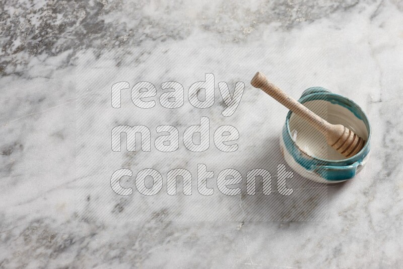 Multicolored pottery bowl with wooden honey dipper in it on grey marble background