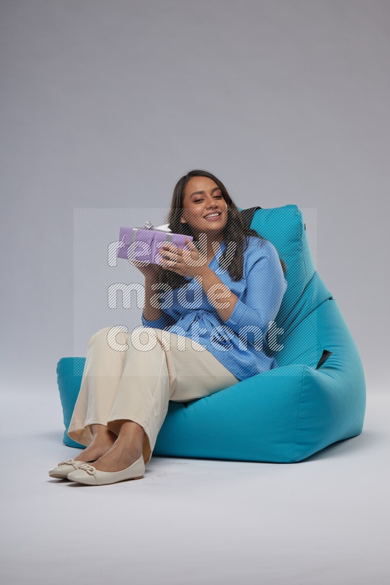 A woman sitting on a blue beanbag and holding a gift
