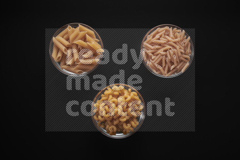 Different pasta types in glass bowls on black background