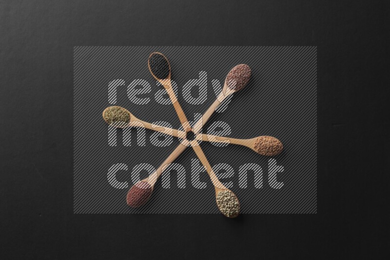 wooden spoons filled with white peppers, mustard seeds, black seeds, garden cress, cumin and flax on black flooring