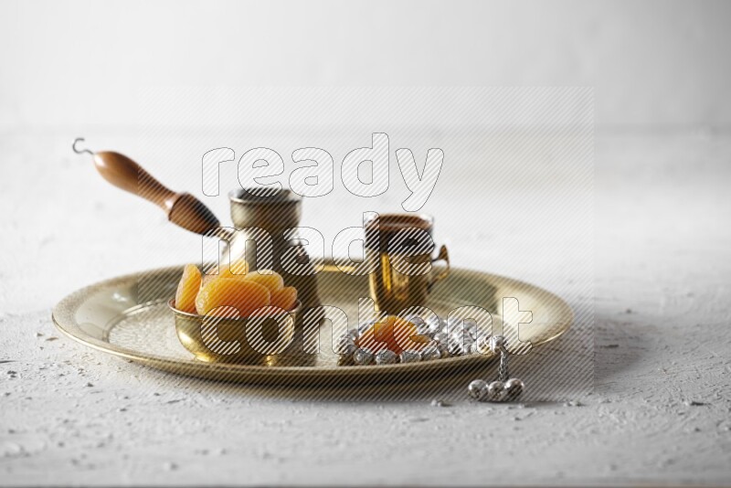 Dried apricots in a metal bowl with coffee and prayer beads on a tray in a light setup