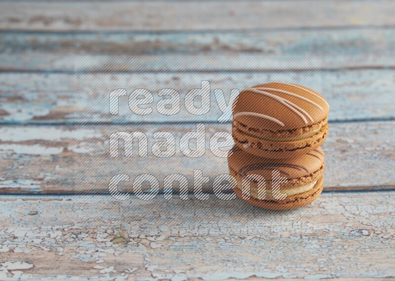 45º Shot of of two assorted Brown Irish Cream, and light brown Almond Cream macarons next to each other on light blue background