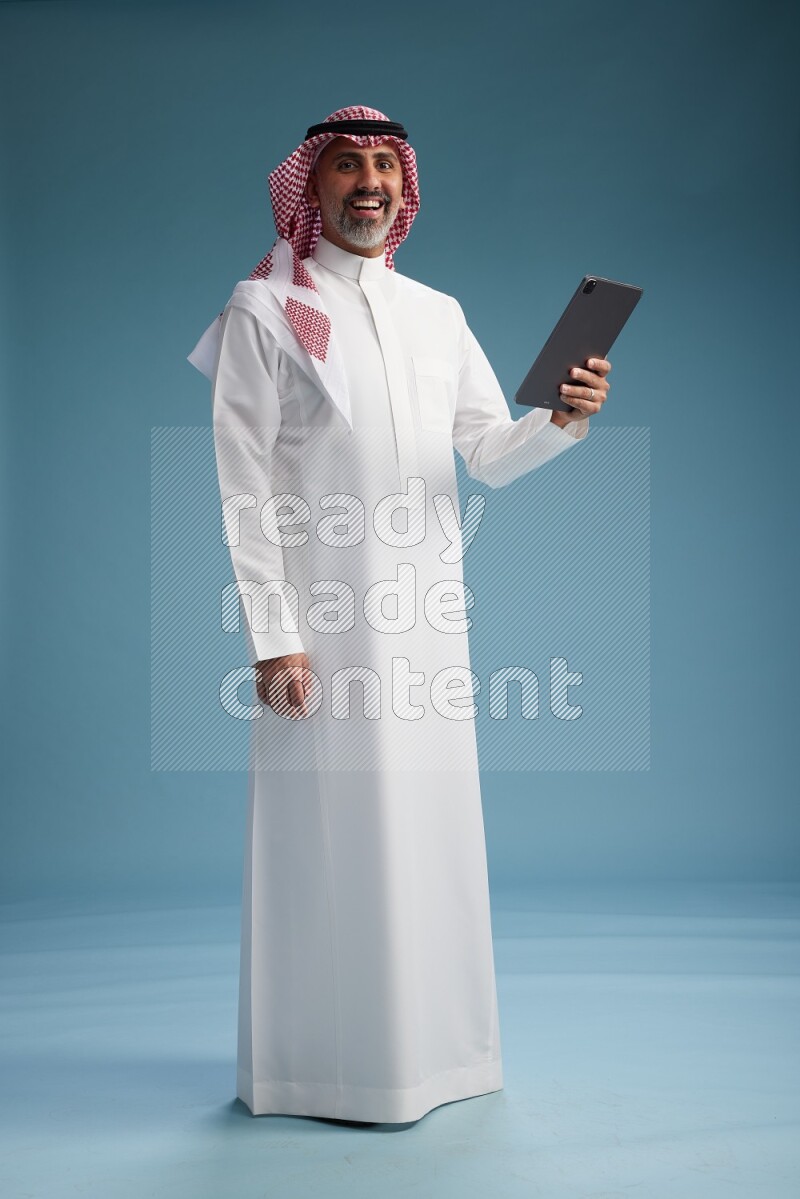 Saudi man wearing thob and shomagh with tablet on Blue background