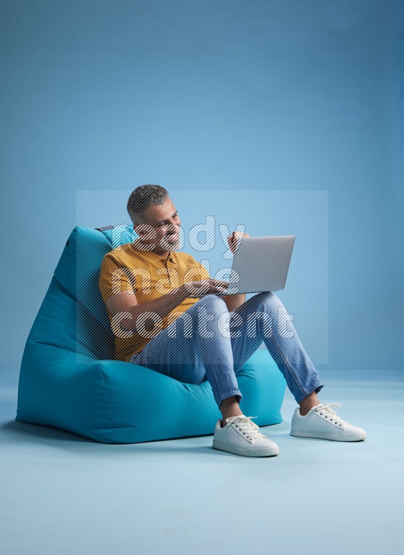 A man sitting on a blue beanbag and working on laptop