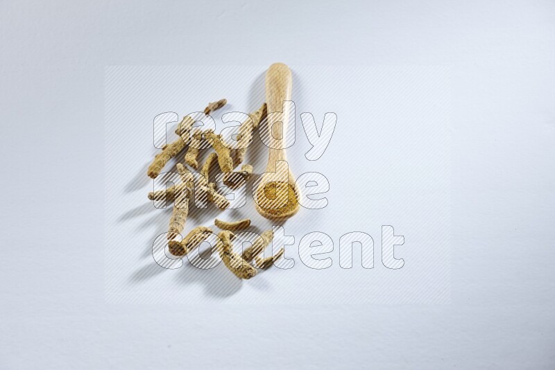 ملعقة خشبية ممتلئة ببودرة الكركم مع أصابع الكركم المجففة بجانبها على خلفية بيضاء