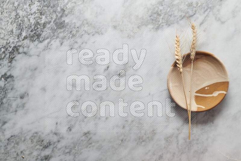 Wheat stalks on multicolored pottery plate on grey marble background