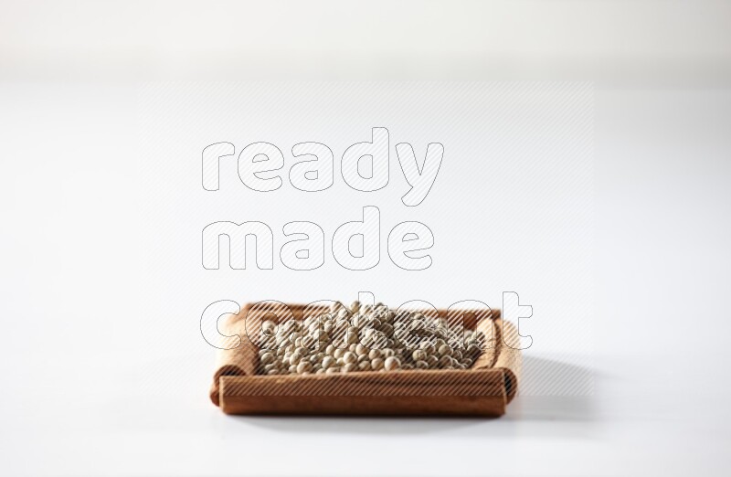 أربعة من أعواد القرفة مكونة شكل مربع بداخلها حبوب الفلفل الأبيض علي خلفية بيضاء