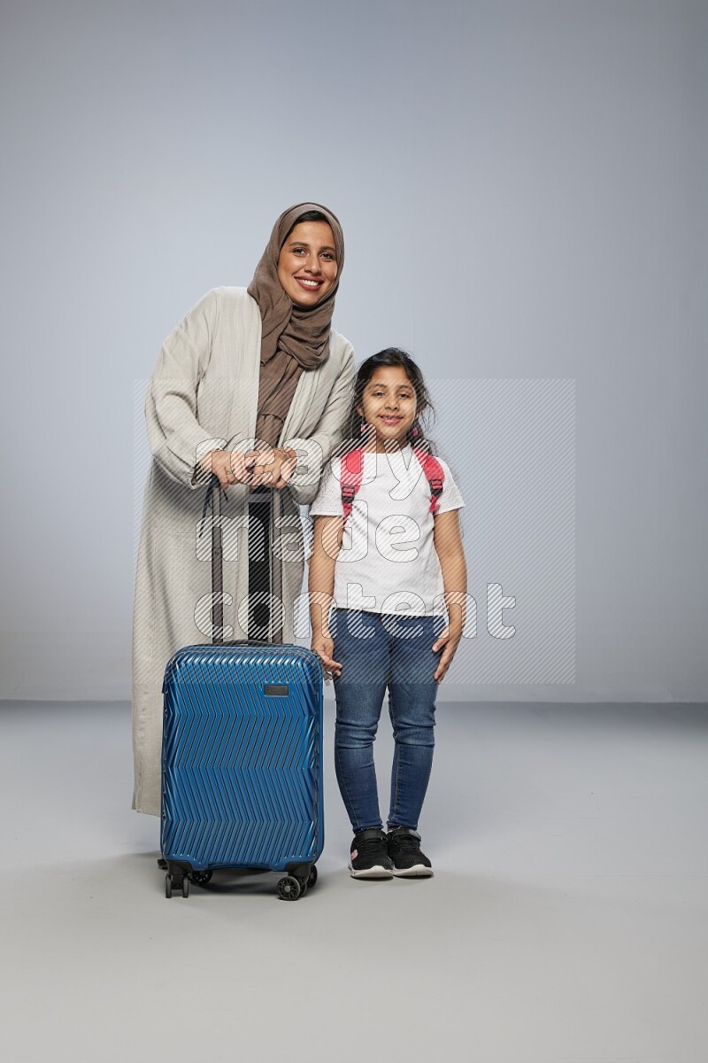 Mom and daughter standing pulling a carry-on bag on gray background
