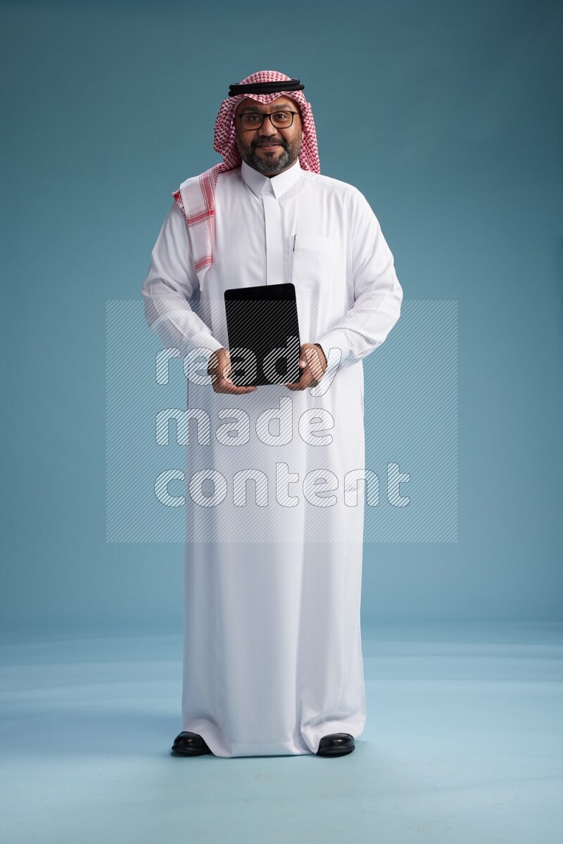 Saudi Man with shimag Standing holding a tablet on blue background