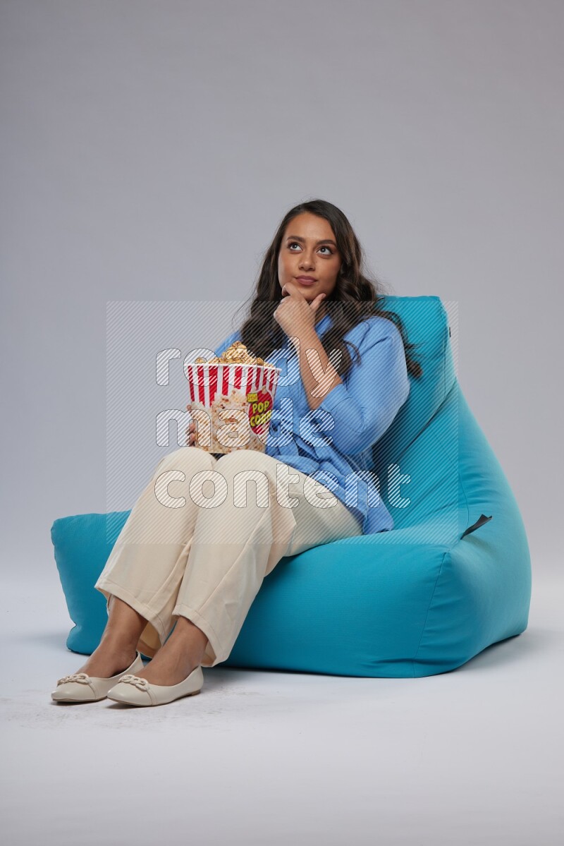 A woman sitting on a blue beanbag and eating popcorn